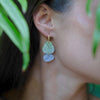 A woman wearing a chic gold hoop earring with two organic acrylic charms in periwinkle blue and marbled sage green.
