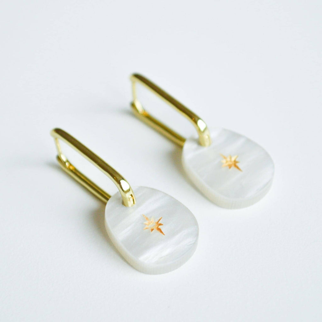 A pair of earrings with stylish square gold hoops and a pearl coloured iridescent acrylic charm with a sweet gold star etched into it. 