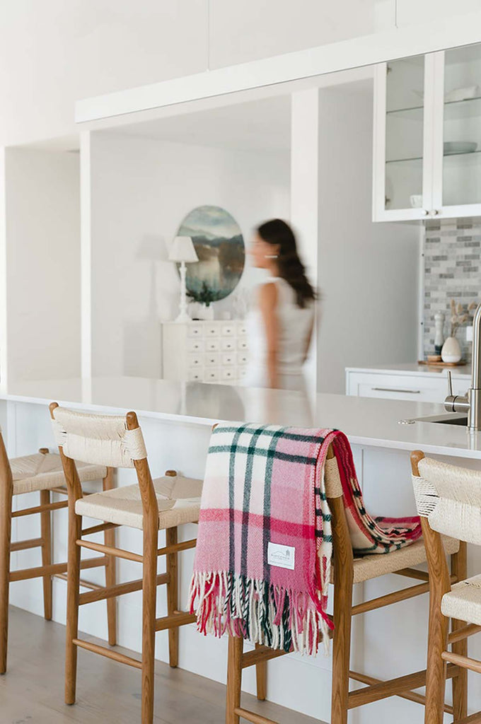 A modern dining room, with a pink check throw blanket by Ruanui Station NZ folded over the side of one of the chairs. 