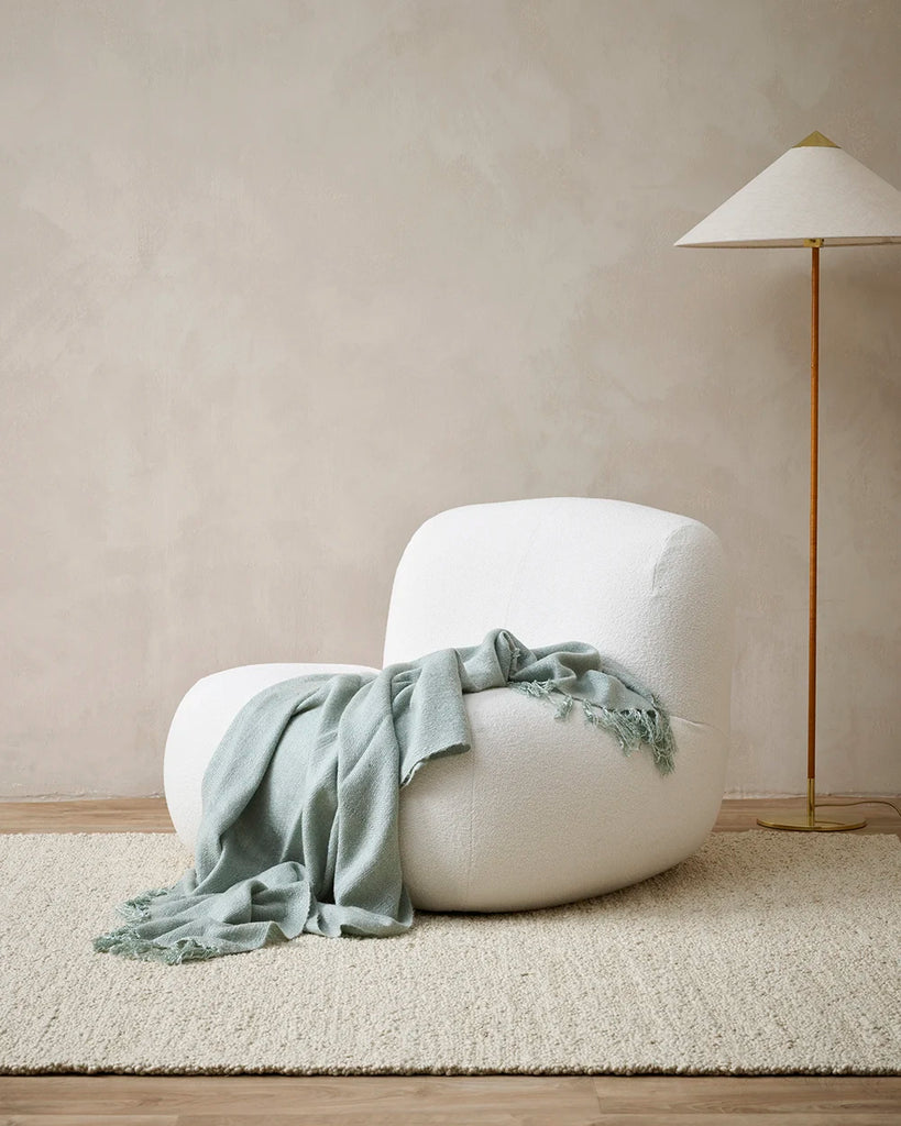 Light grey wool-blend throw blanket with tasseled fringe, drpaed over a chair in a modern living room