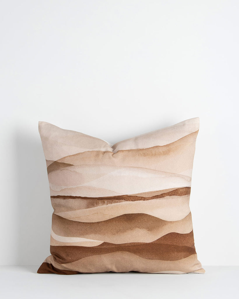 A printed cushion with dune-like watercolour patterns in shades of desert brown, burnt sienna and umber. By Baya