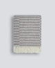 An off-set striped patterned throw blanket in shades of warm beige and oatmeal, with a twisted fringe edge in 100% NZ wool by Baya