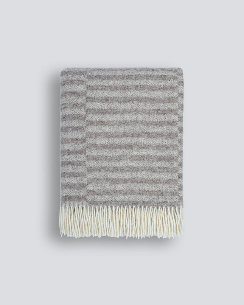 An off-set striped patterned throw blanket in shades of warm beige and oatmeal, with a twisted fringe edge in 100% NZ wool by Baya