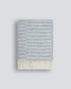 An off-set striped patterned throw blanket in shades of cool silver and pale blue, with a twisted fringe edge in 100% NZ wool by Baya
