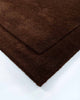 The corner of the Norfolk floor rug in the shade Chocolate. The border of the rug is cut-pile in a minimalist and refined design. 