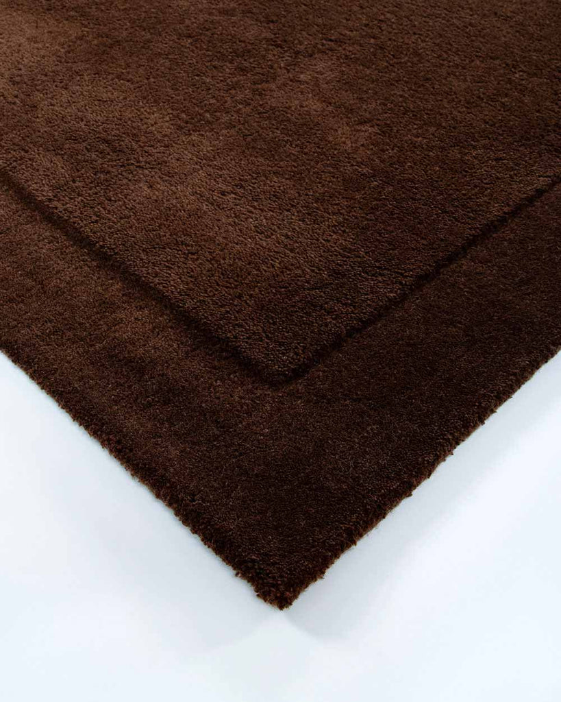 The corner of the Norfolk floor rug in the shade Chocolate. The border of the rug is cut-pile in a minimalist and refined design. 