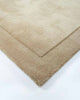 A corner view of the luxurious Norfolk rug in the shade Sand, a warm beige. The cut-pile border lends a sense of minimalism to this sumptous, 100% wool floor rug. 