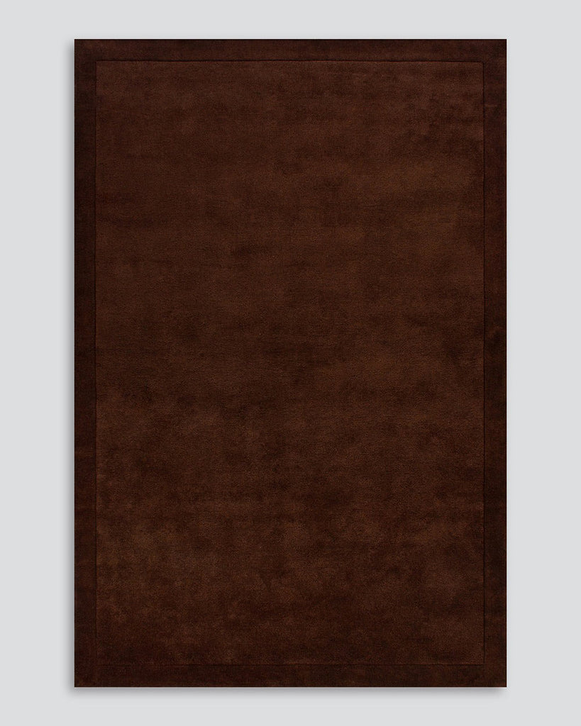 A full image of the Norfolk floor rug in the shade Chocolate. The border of the rug is cut-pile in a minimalist and refined design, and the pile of the rug's centre is luxuriously deep. 