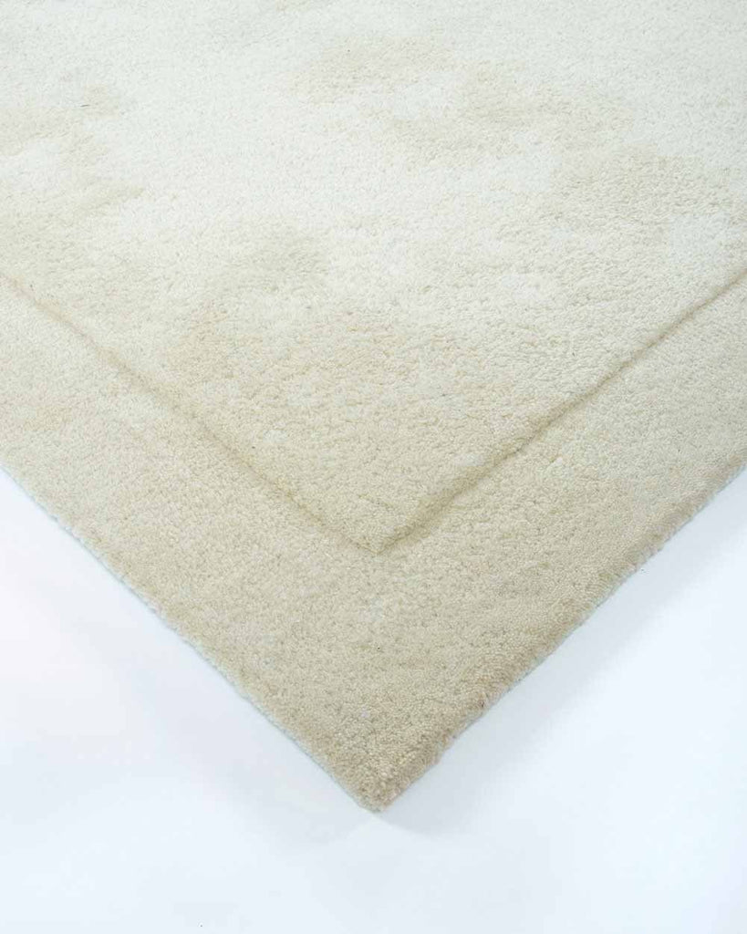 The corner of the Norfolk floor rug in Ivory. The minimalist cut-pile of the edges adds interest to this luxurious, 100% wool piece. 