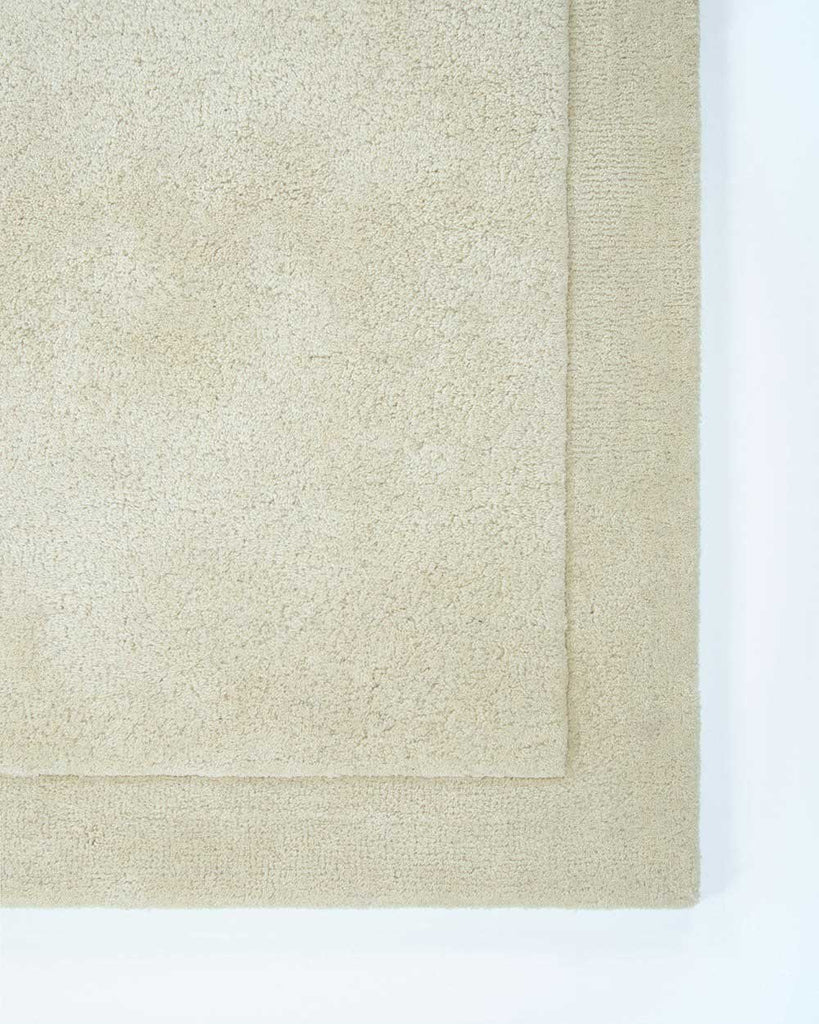 The corner of the Norfolk floor rug in the shade Ivory. The border of the rug is cut-pile in a minimalist and refined design. 
