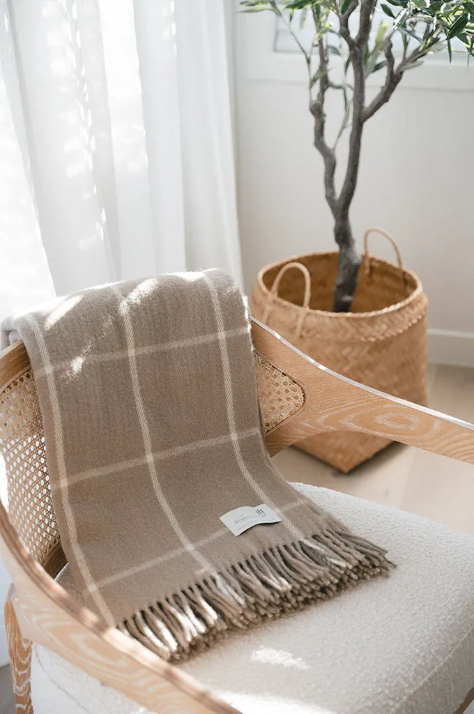 A New Zealand wool throw blanket, in a simple beige-brown check, draped over a chair