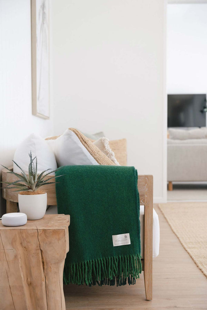 A deep green lambswool throw blanket from Ruanui Station NZ, folded on a couch in a modern living room. 