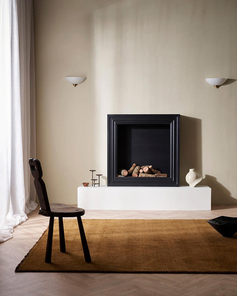 A rich warm brown 100% wool floor rug in front of a cosy looking fireplace. 
