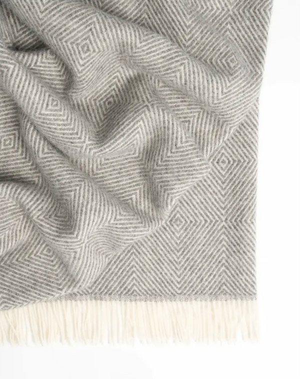 A soft grey wool throw blanket in a large size, featuring a traditional Scandinavian design and fringe