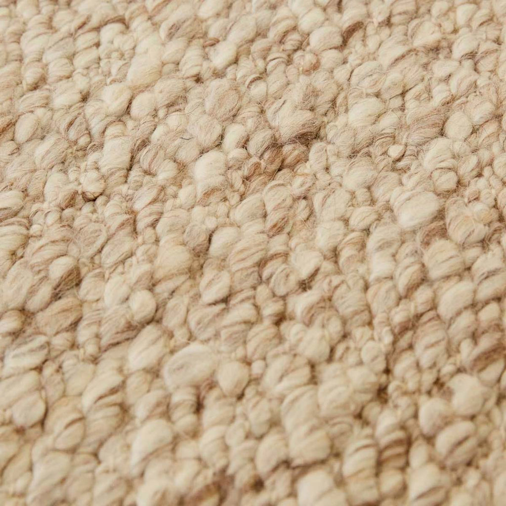 Close up of the weave of a textural wool blend boucle style rug by Globe West and Soren Liv NZ in shades of warm beige and light brown.