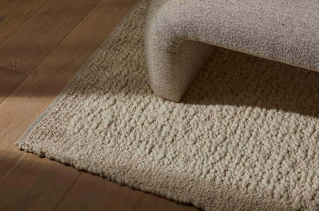 A textural wool blend boucle style rug by Globe West and Soren Liv NZ in shades of warm ivory and cream, situated underneath a designer couch. 