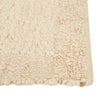 Close up of the corner of a textural wool blend boucle style rug by Globe West and Soren Liv NZ in shades of warm ivory and cream. The edge of the rug is indented, adding interest.