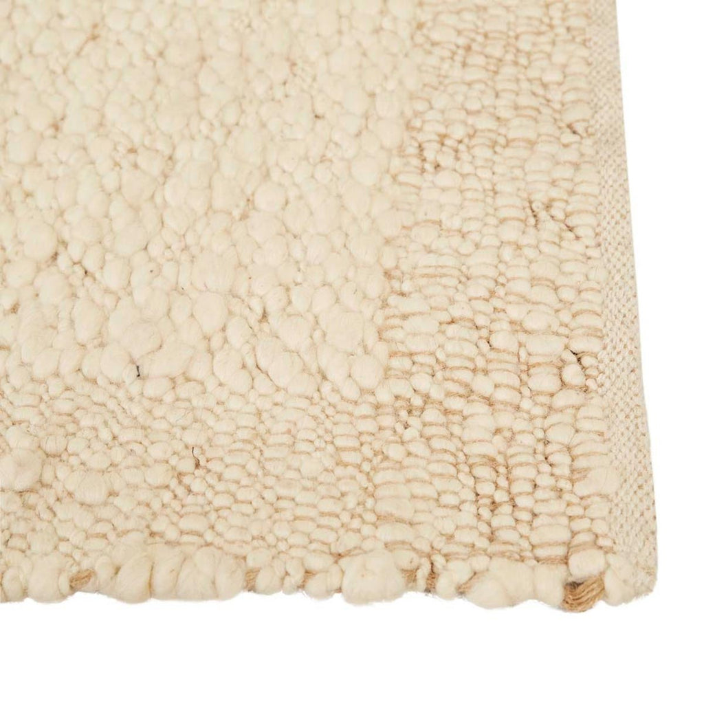 Close up of the corner of a textural wool blend boucle style rug by Globe West and Soren Liv NZ in shades of warm ivory and cream. The edge of the rug is indented, adding interest.