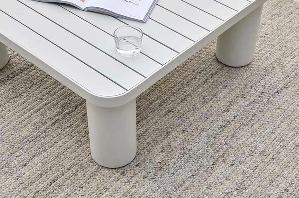 A handknotted rug by Globe West and Soren Liv NZ in neutral grey beige tones, perfect for outdoors or transition spaces, situated under an outdoor table. 