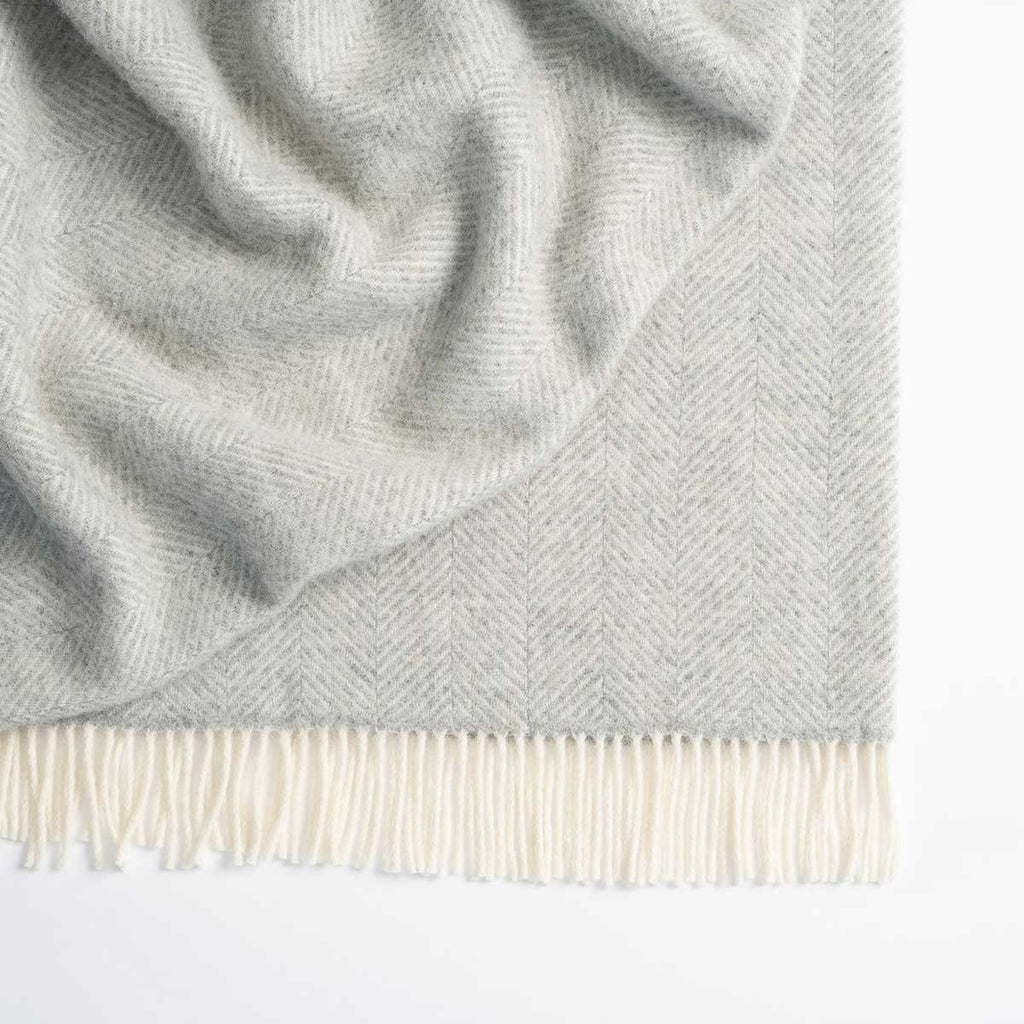 A soft grey and white herringbone throw blanket designed by Weave Home, with a white fringed border. 