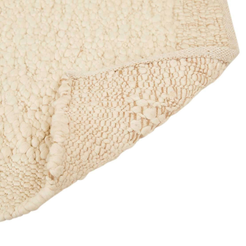 Close up of the corner of a textural wool blend boucle style rug by Globe West and Soren Liv NZ in shades of warm ivory and cream. The edge of the rug is flipped up, showing the underside. 